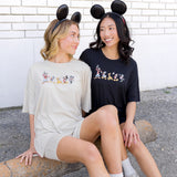 2 women wearing biker short sets in a cream and black colorway with mickey and friend graphic and wearing mickey mouse ear headbands