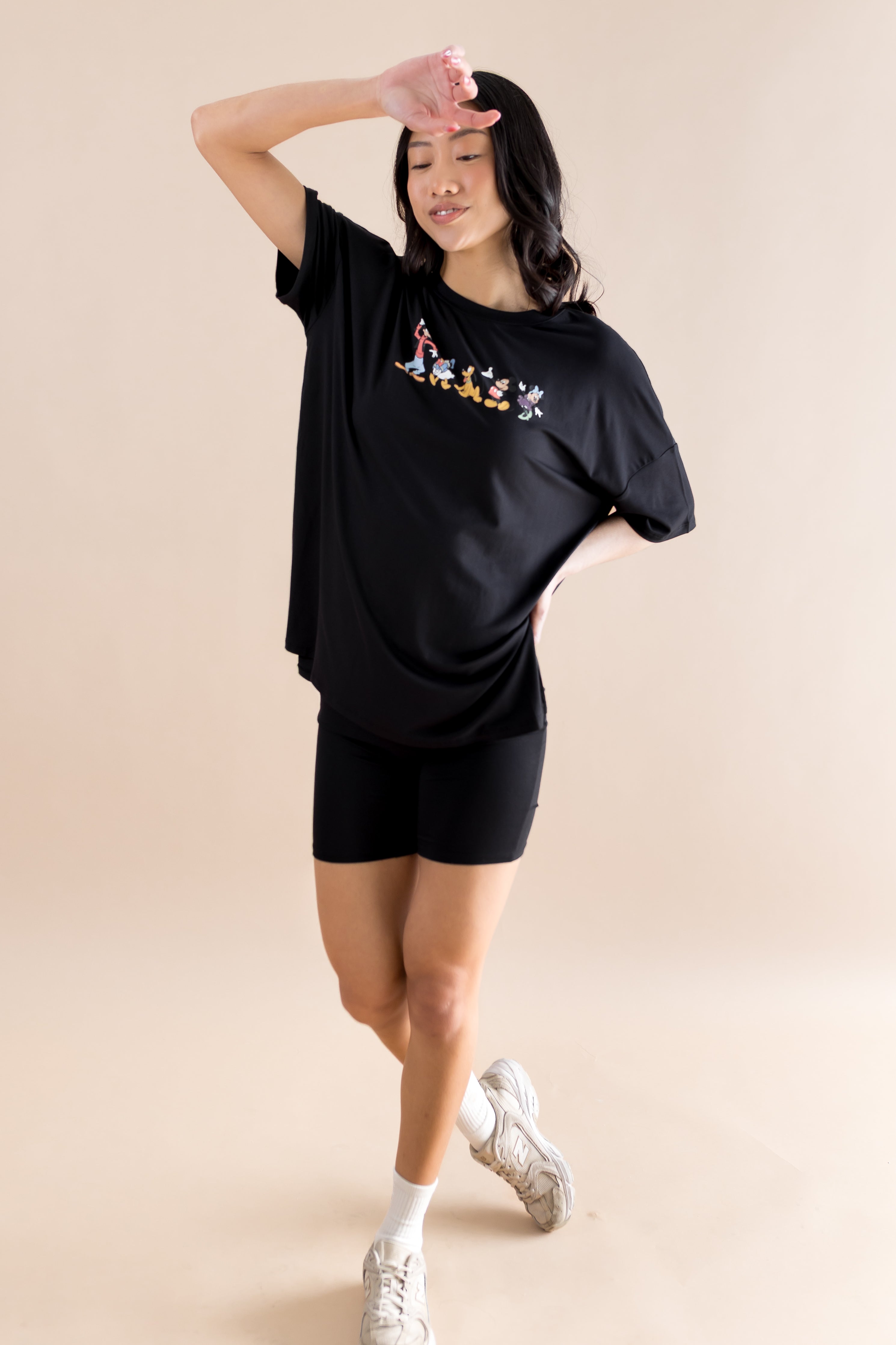 Model with arm on her forehead while wearing the Women’s Biker Short Set in Mickey and Friends on Midnight paired with white sneakers