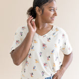 Model smiling to the side with one hand in her pocket while wearing the Women's Relaxed Fit V-Neck in Mickey Mouse and Friends