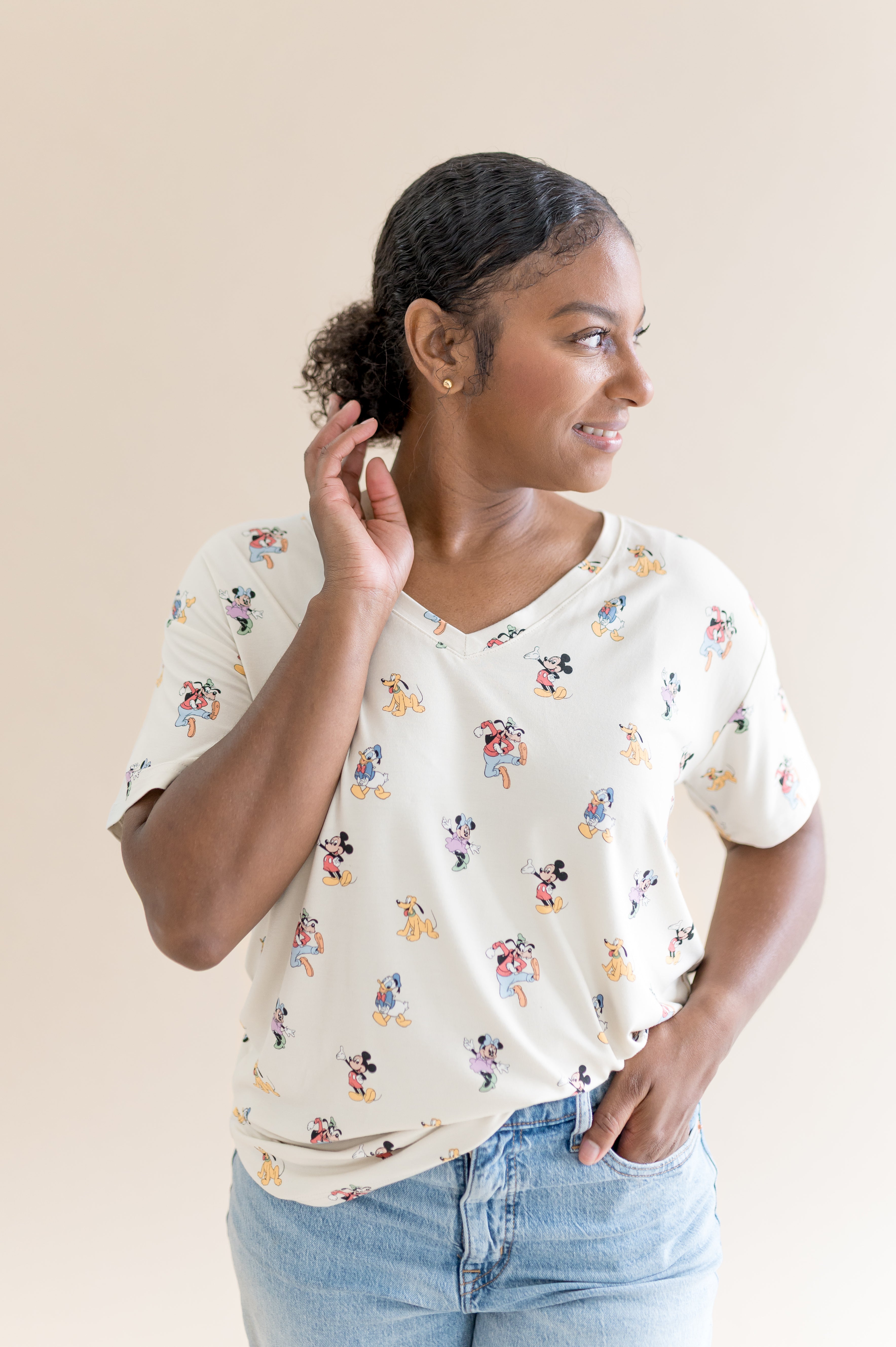Model smiling to the side with one hand in her pocket while wearing the Women's Relaxed Fit V-Neck in Mickey Mouse and Friends