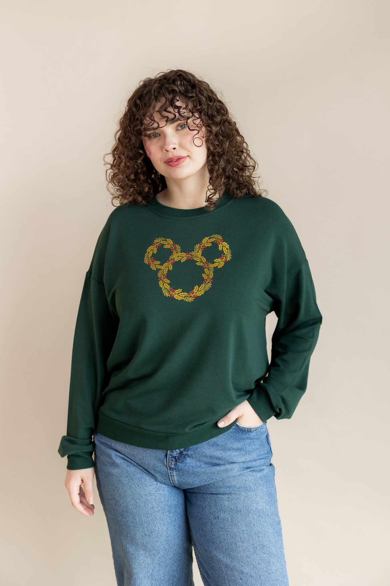 Women wearing Women's Sweatshirt in Mickey Christmas Wreath print on Cypress color on blue jeans on a beige background
::: Model is 5'10" wearing size XL ///