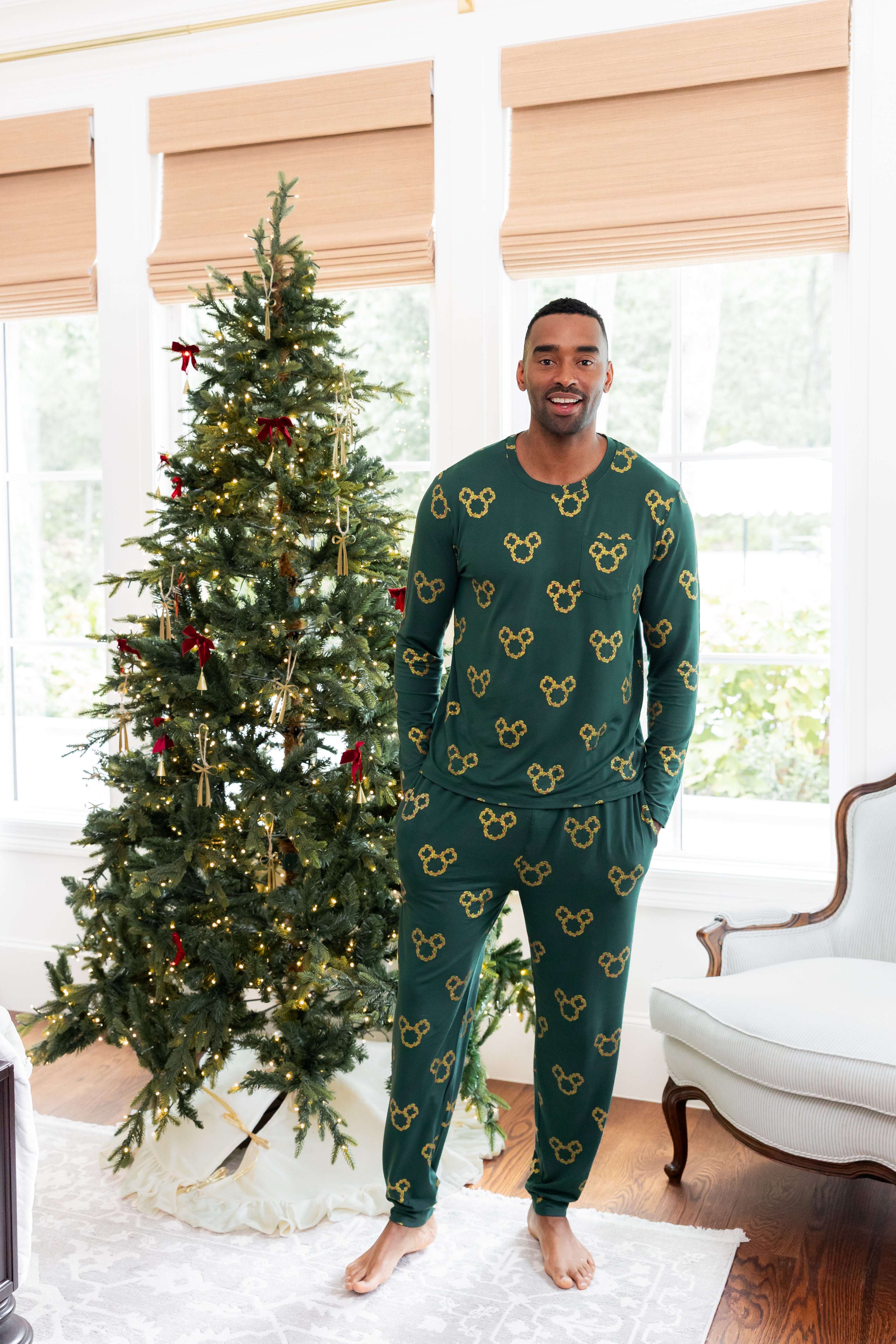 Man standing in front of decorated Christmas tree wearing Men's Jogger Set in Mickey Christmas Wreath print