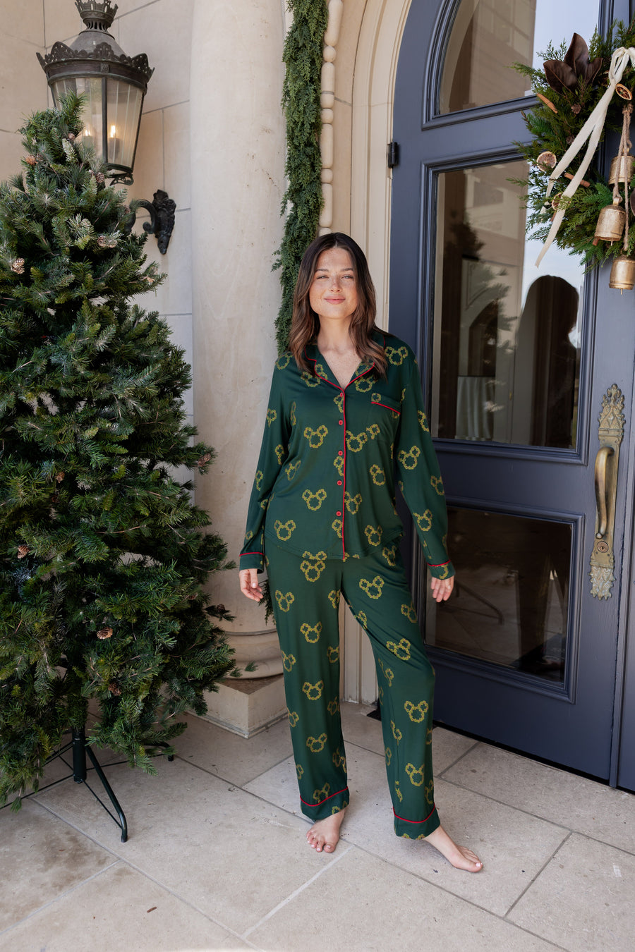 Woman wearing Long-Sleeved Women's Pajama Set in Mickey Christmas Wreath print smiling outdoors beside a Christmas tree