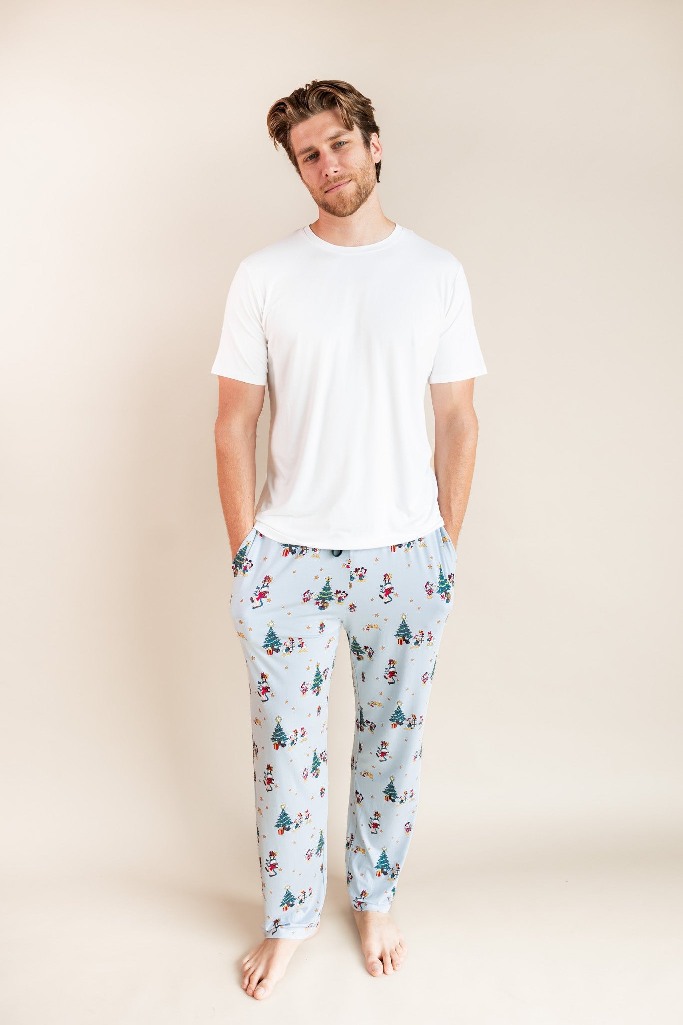 Man wearing Men's Lounge Pants in Mickey & Friends Christmas print over white T-shirt on a beige background