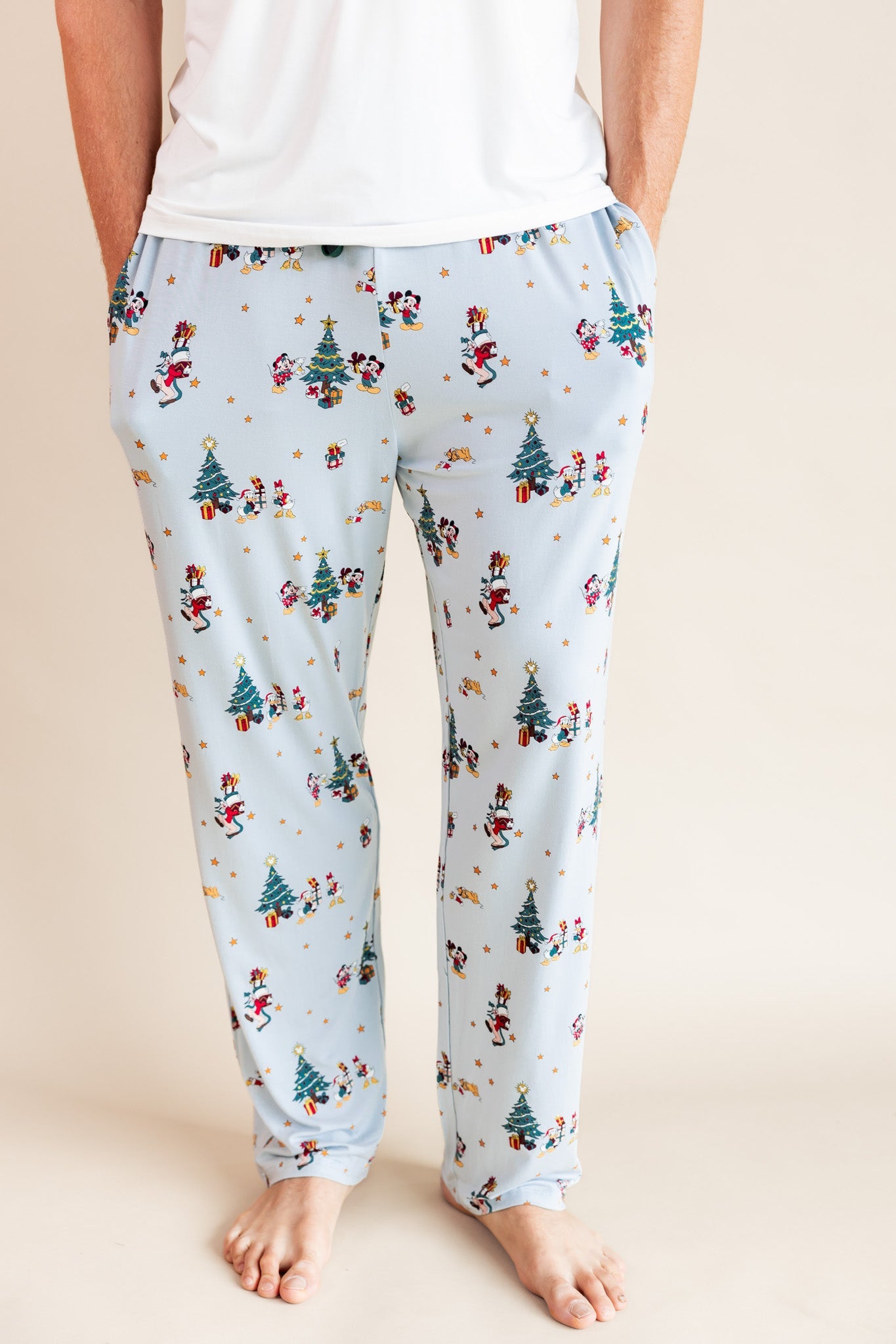Man wearing Men's Lounge Pants in Mickey & Friends Christmas print with pockets over white T-shirt on a beige background