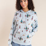 Woman wearing Women's Hoodie in Mickey & Friends Christmas print on blue jeans on a beige background