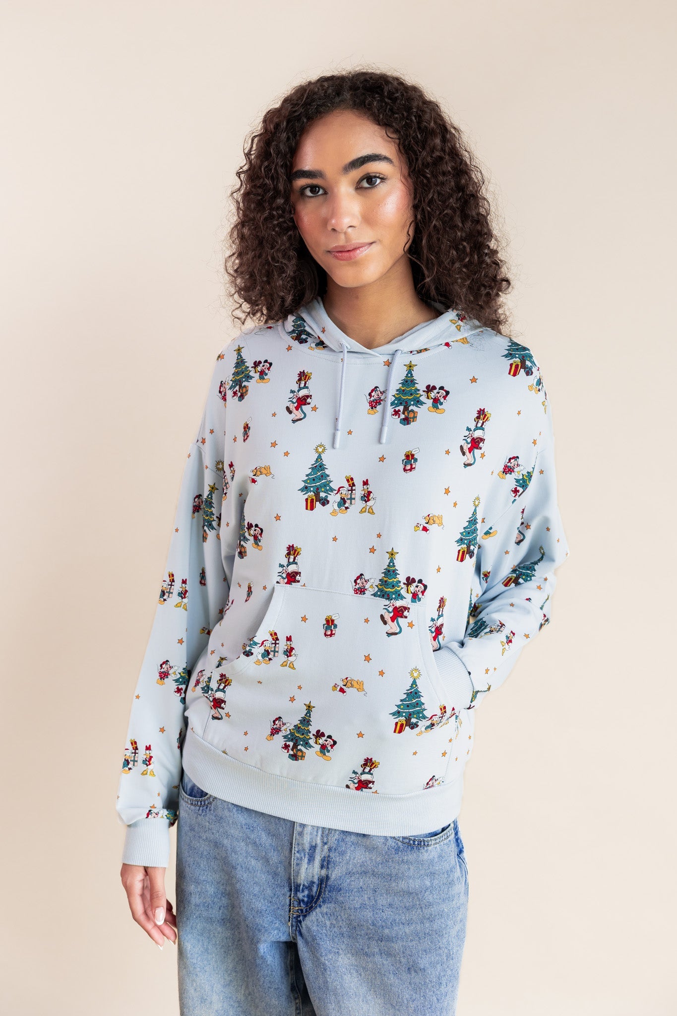 Woman wearing Women's Hoodie in Mickey & Friends Christmas print on blue jeans on a beige background
