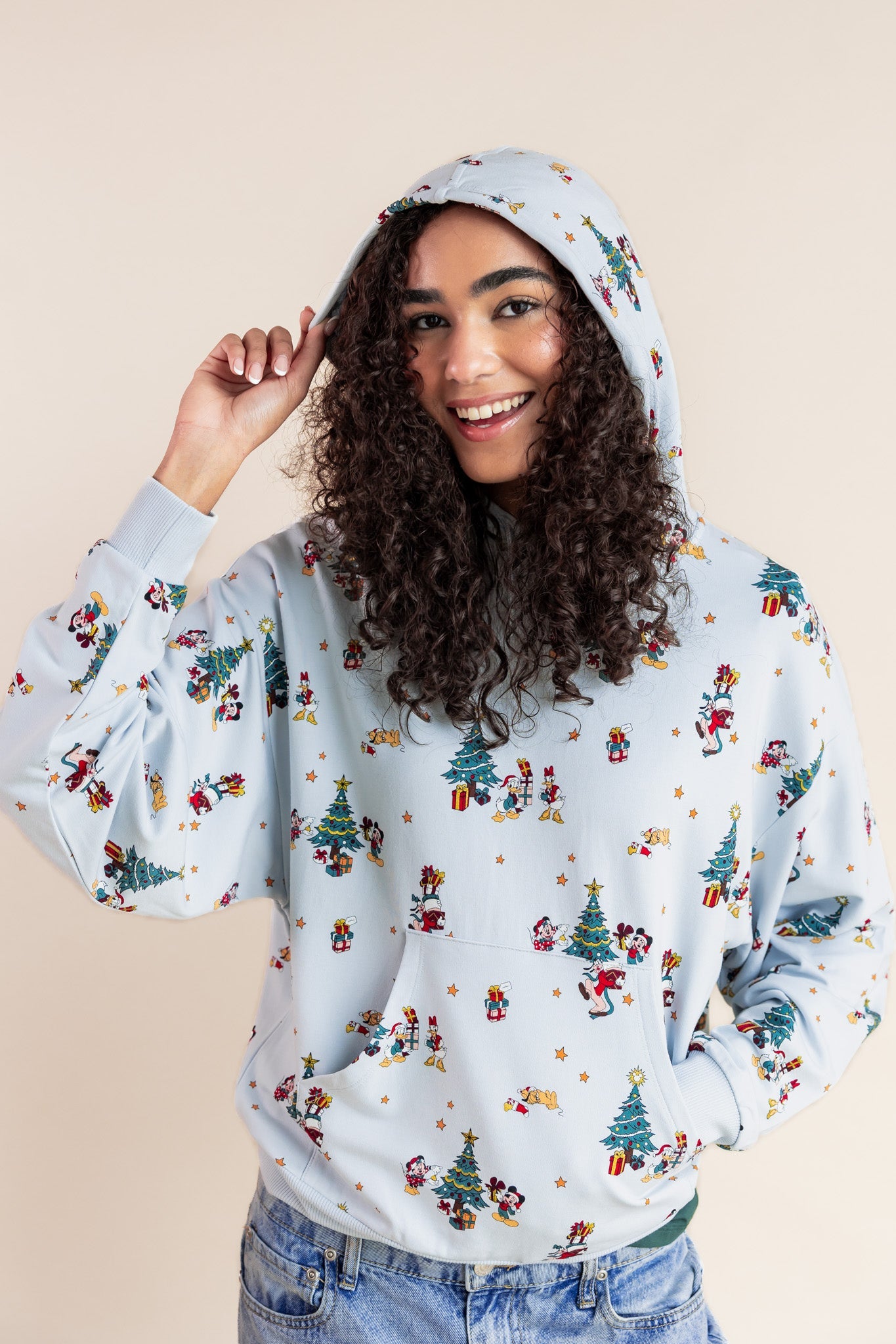 Woman wearing Women's Hoodie in Mickey & Friends Christmas print on blue jeans on a beige background
::: Model is 5'10" wearing size XS ///