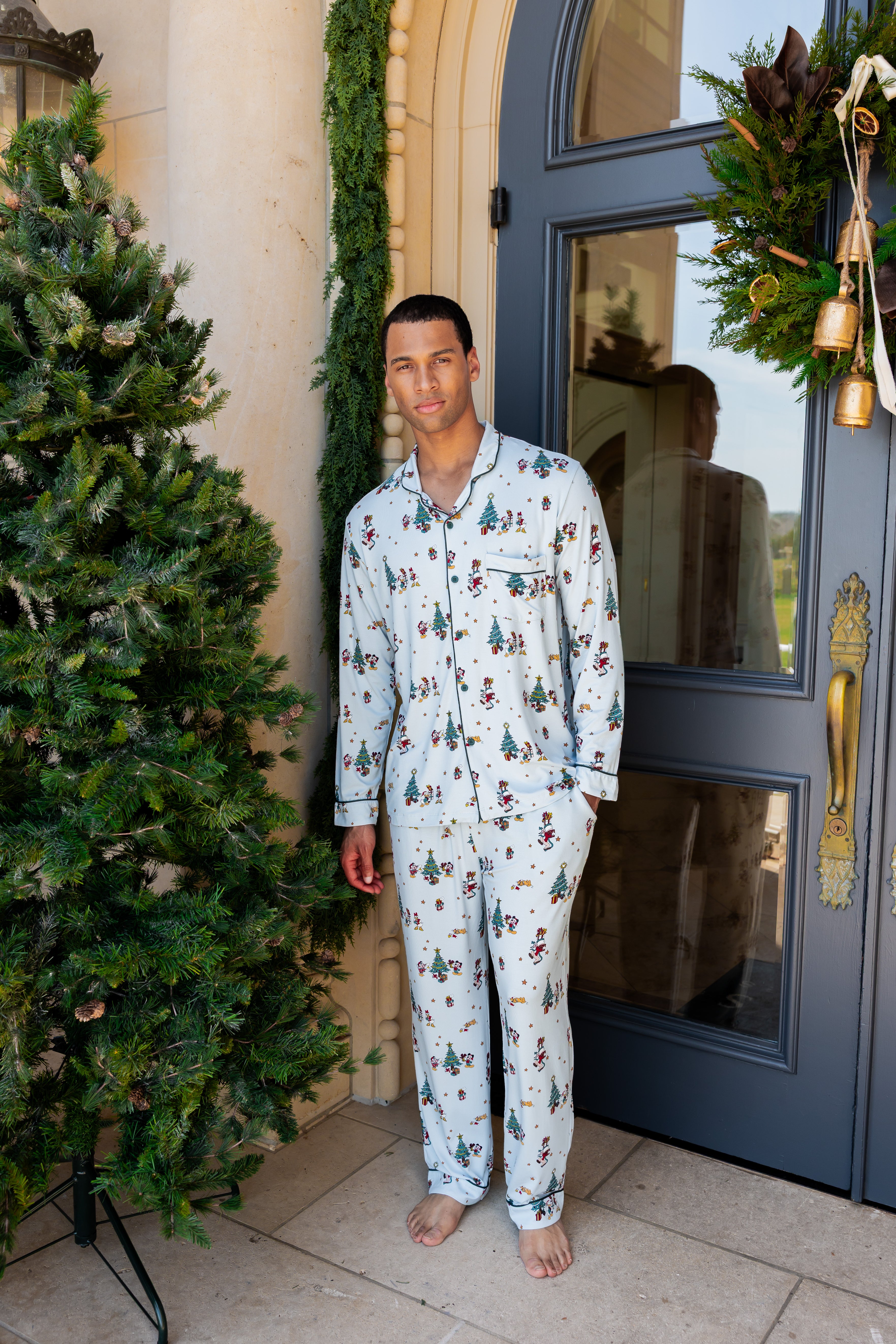 male model wearing holiday mickey printed blue pajama set on a porch decorated with christmas decor
