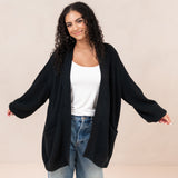 Woman wearing a black cardigan over a white top and blue jeans on a beige background