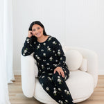 Woman sitting on a white chair wearing a Big Midnight Magnolia jogger set in a minimalistic room.