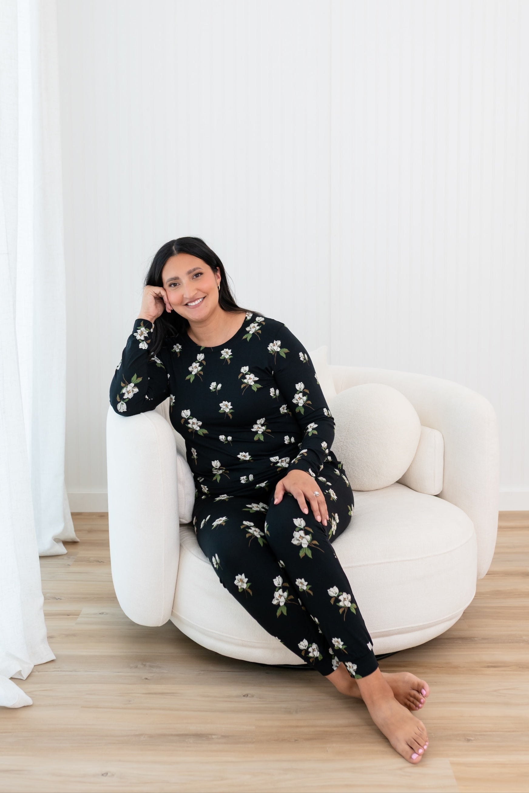 Woman sitting on a white chair wearing a Big Midnight Magnolia jogger set in a minimalistic room.