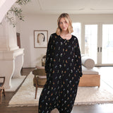 Model standing in a light modern bohemian room while wearing the Long Sleeve Adult Sleep Bag Walker in Midnight Wildflower with her hands in her pocket ::: Model is 5'10" wearing size XS ///