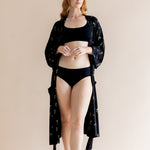 Model wearing black bra and underwear with Women’s Kimono Robe in Midnight Wildflower print on a beige background