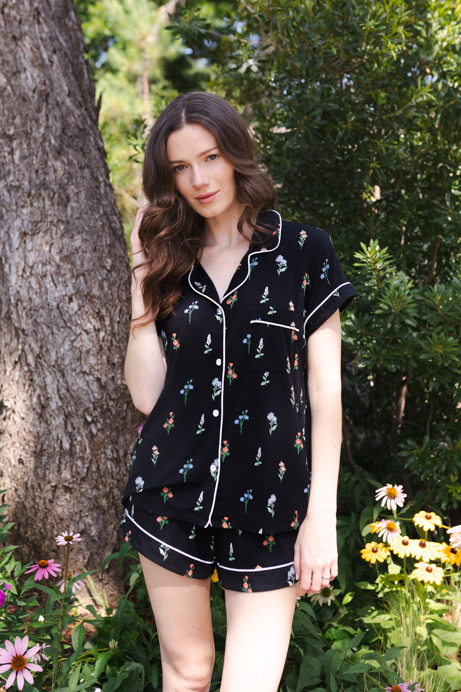 Model standing in front of a tree and greenery while wearing the Women's Short Sleeve Pajama Set in Midnight Wildflower
