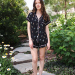 Brunette model standing on a stone walkway in a garden while wearing the Women's Short Sleeve Pajama Set in Midnight Wildflower ---PJ 2