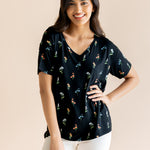 Model posing in Women's Relaxed Fit V-Neck in Midnight Wildflower print over white pants on a beige background
