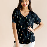 Model posing in Women's Relaxed Fit V-Neck in Midnight Wildflower print over white pants on a beige background