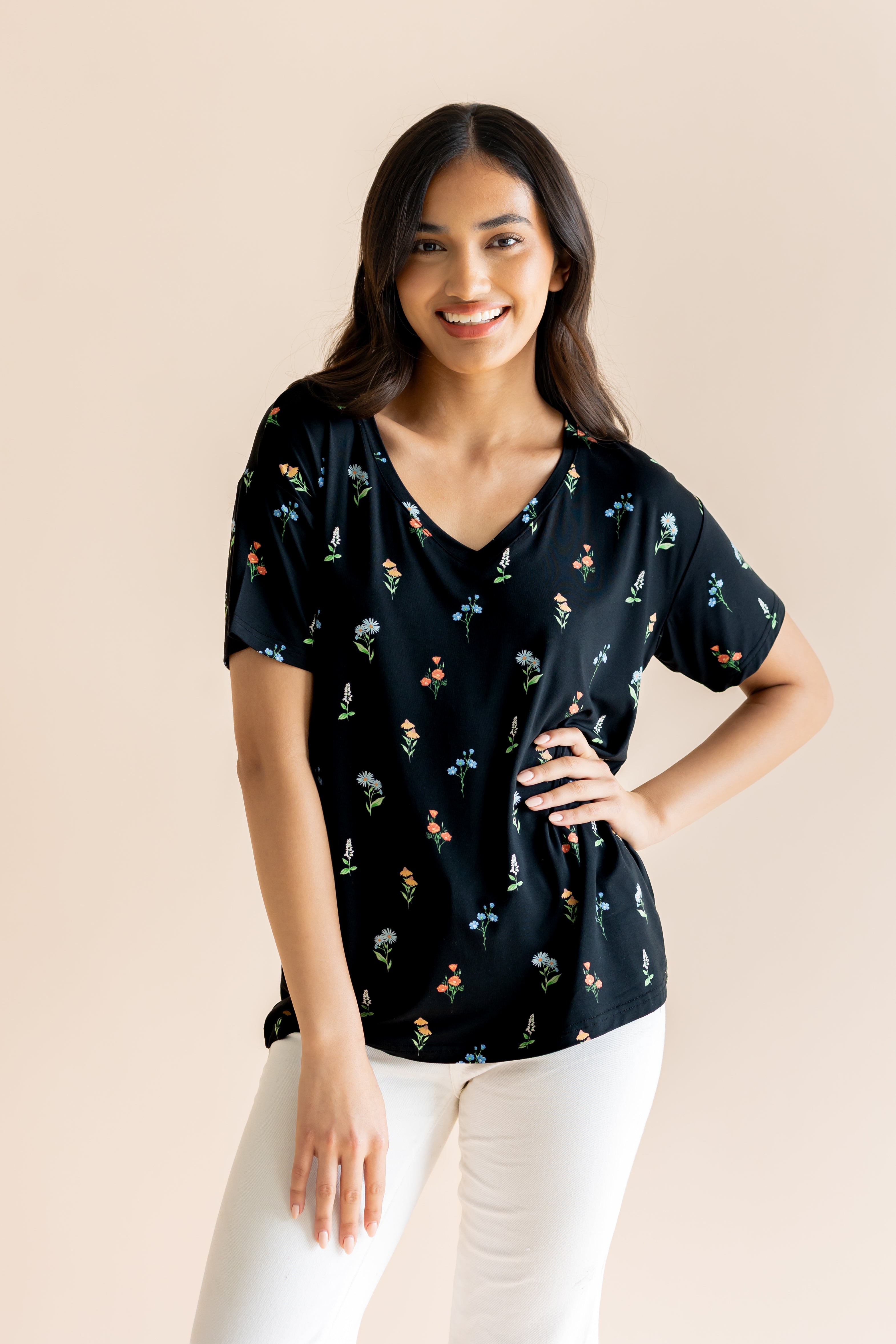 Model posing in Women's Relaxed Fit V-Neck in Midnight Wildflower print over white pants on a beige background