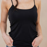 Person wearing a black tank top and blue jeans against a beige background