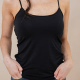 Person wearing a black tank top and blue jeans against a beige background
