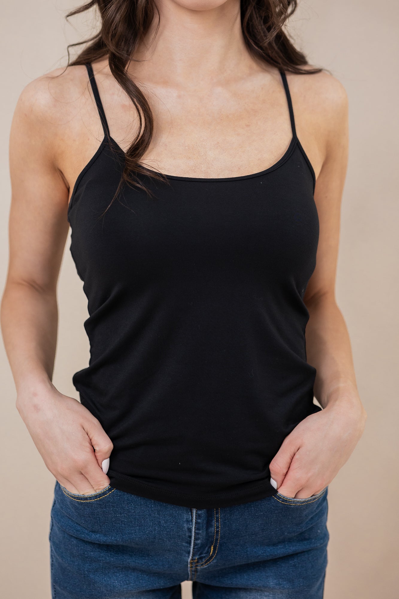 Person wearing a black tank top and blue jeans against a beige background