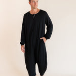 A man modeling a black long-sleeve harem-style sleep sack against a plain beige studio background.