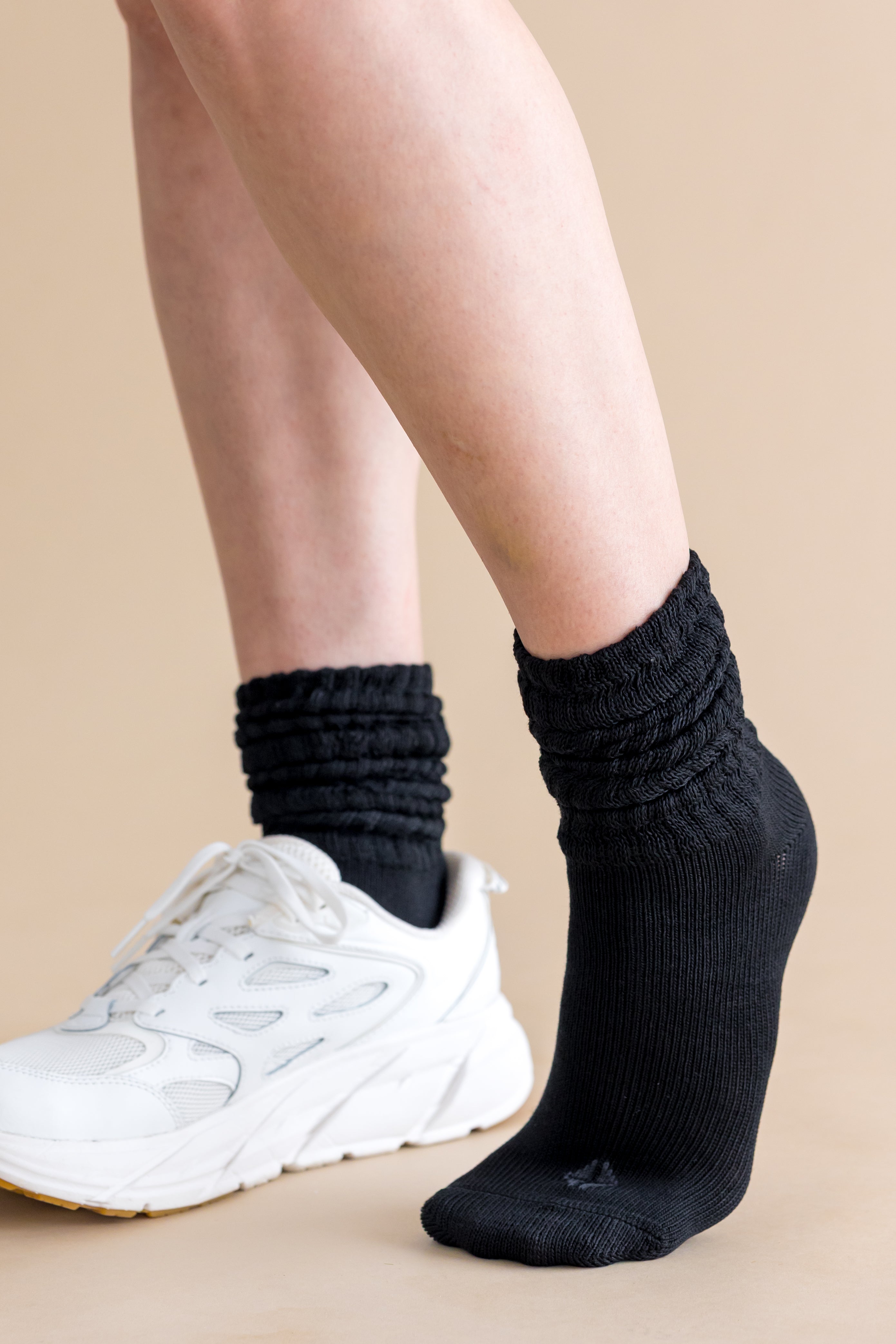 Person wearing black socks and white sneakers on a beige background