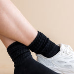 Person wearing black socks with a white sneaker on a beige background