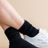 Person wearing black socks with a white sneaker on a beige background