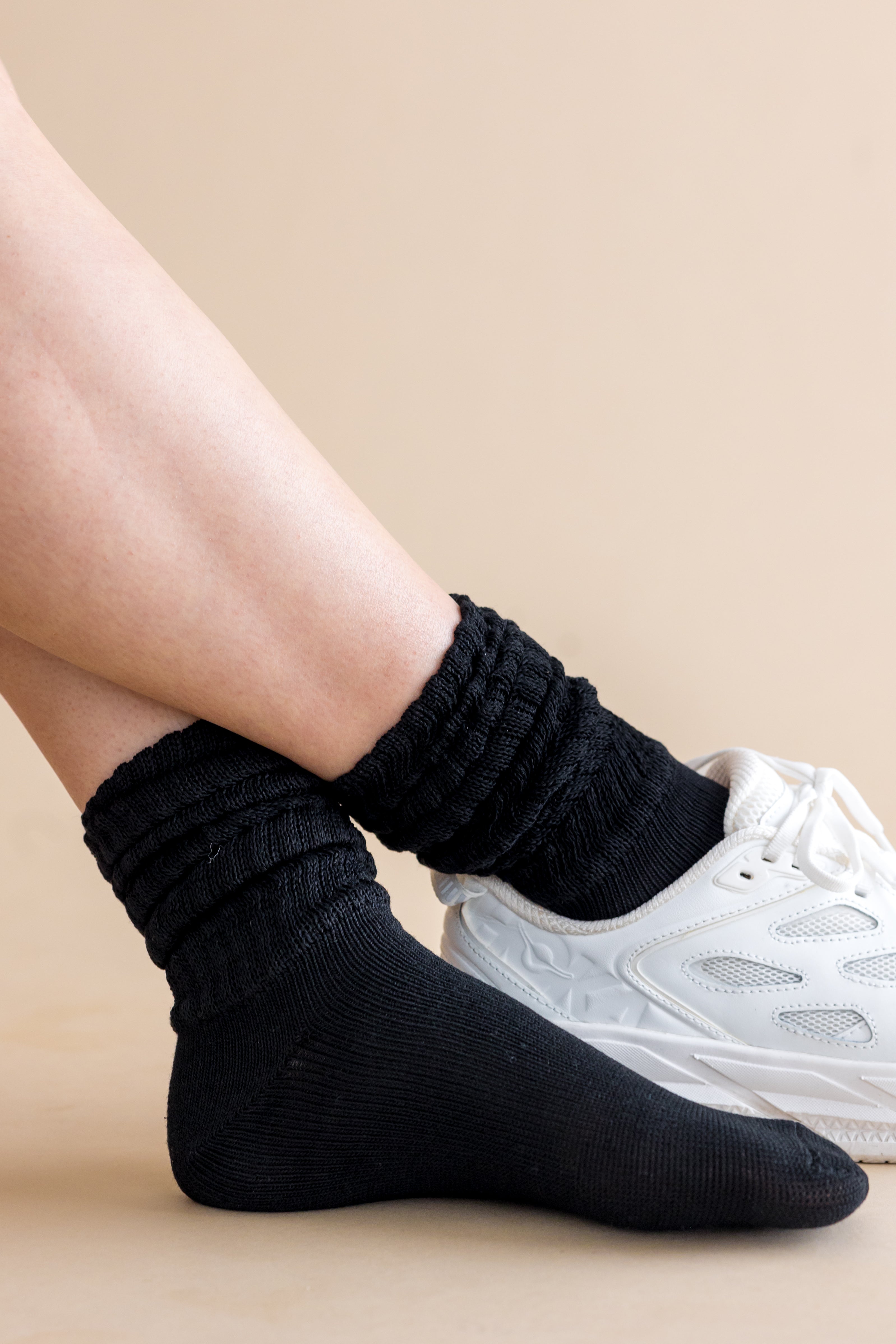 Person wearing black socks with a white sneaker on a beige background