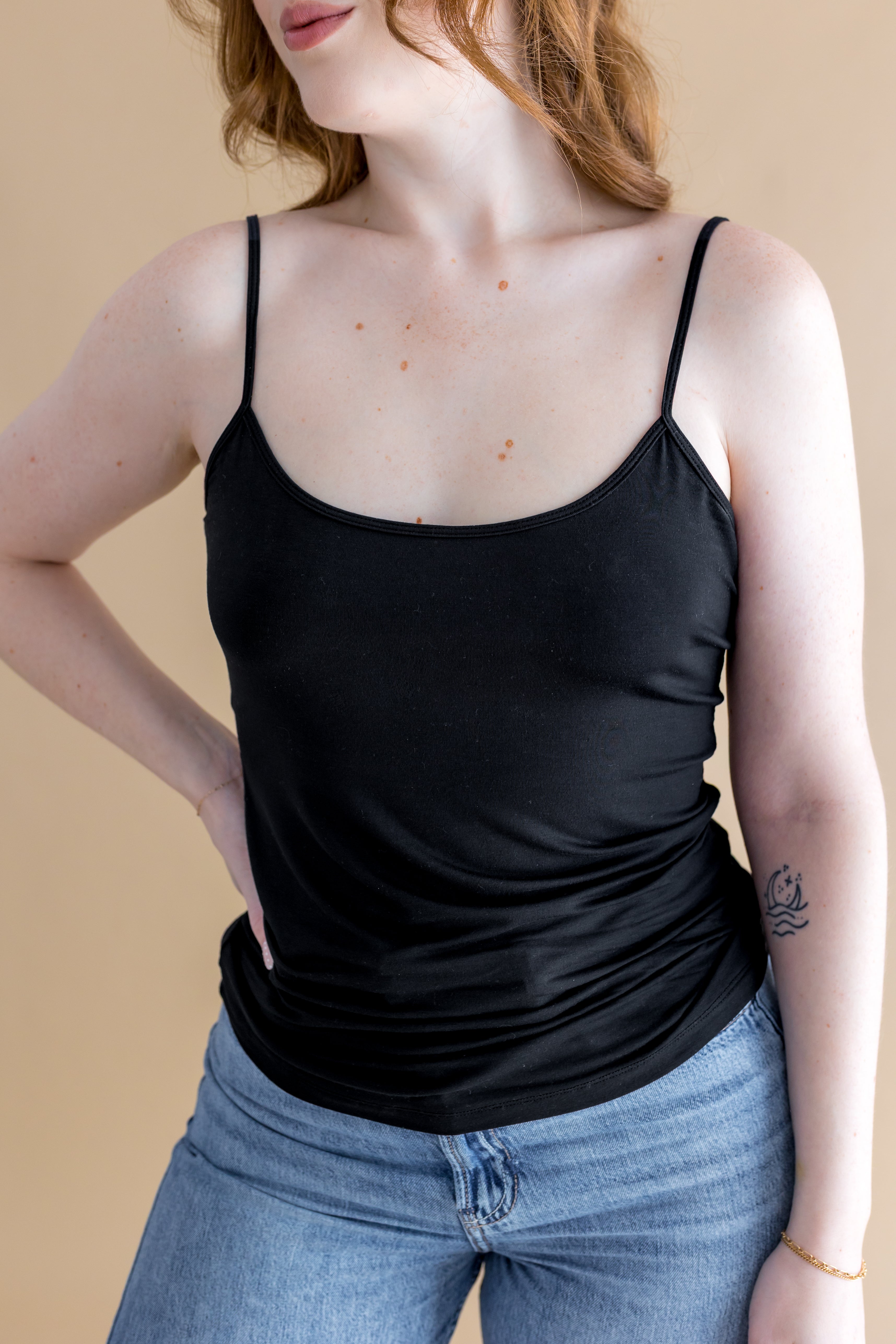 Person wearing a black tank top and blue jeans against a beige background ::: Model is 5'7" wearing size M ///