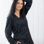 Woman leaning against a cream chair wearing black button up pajamas in a monochromatic leopard print
