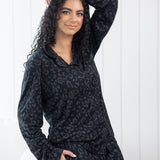 Woman leaning against a cream chair wearing black button up pajamas in a monochromatic leopard print