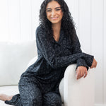 Woman sitting in cream chair wearing black button up pajamas in a monochromatic leopard print
