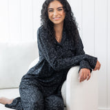 Woman sitting in cream chair wearing black button up pajamas in a monochromatic leopard print