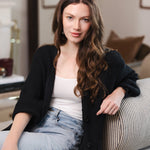 Modal posing on a sofa in a living room wearing Chunky Knit Women's Waffle Cardigan in Midnight over white camisole and blue jeans