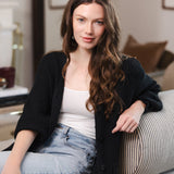 Modal posing on a sofa in a living room wearing Chunky Knit Women's Waffle Cardigan in Midnight over white camisole and blue jeans