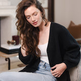 Modal sitting on a sofa in a living room wearing Chunky Knit Women's Waffle Cardigan in Midnight over white camisole and blue jeans