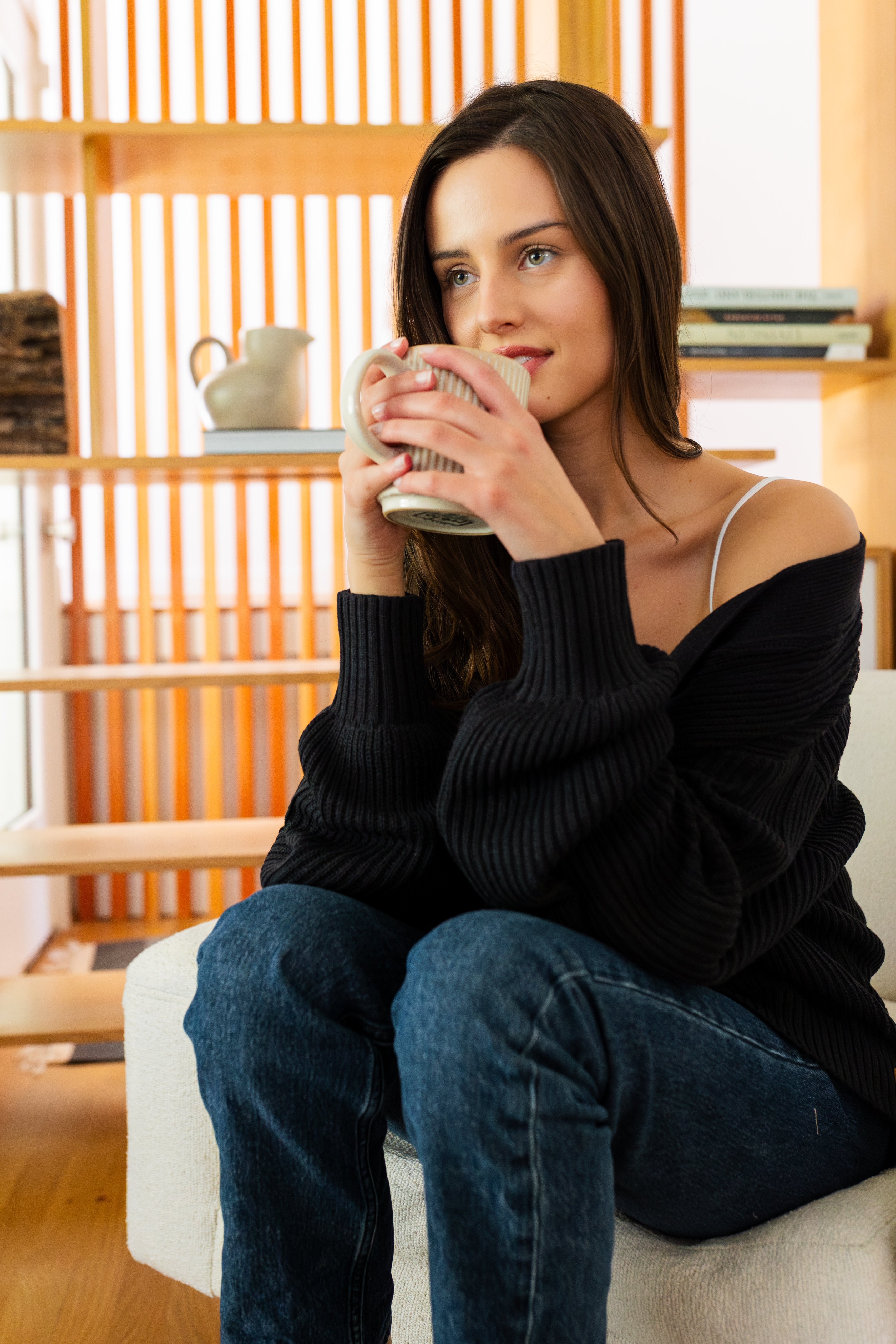 Woman sitting on a couch holding a mug in a cozy living room.