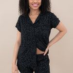 Woman modeling Women’s Short Sleeve Pajama Set in Midnight Leopard with bottom buttons unbuttoned to show the waist band of shorts