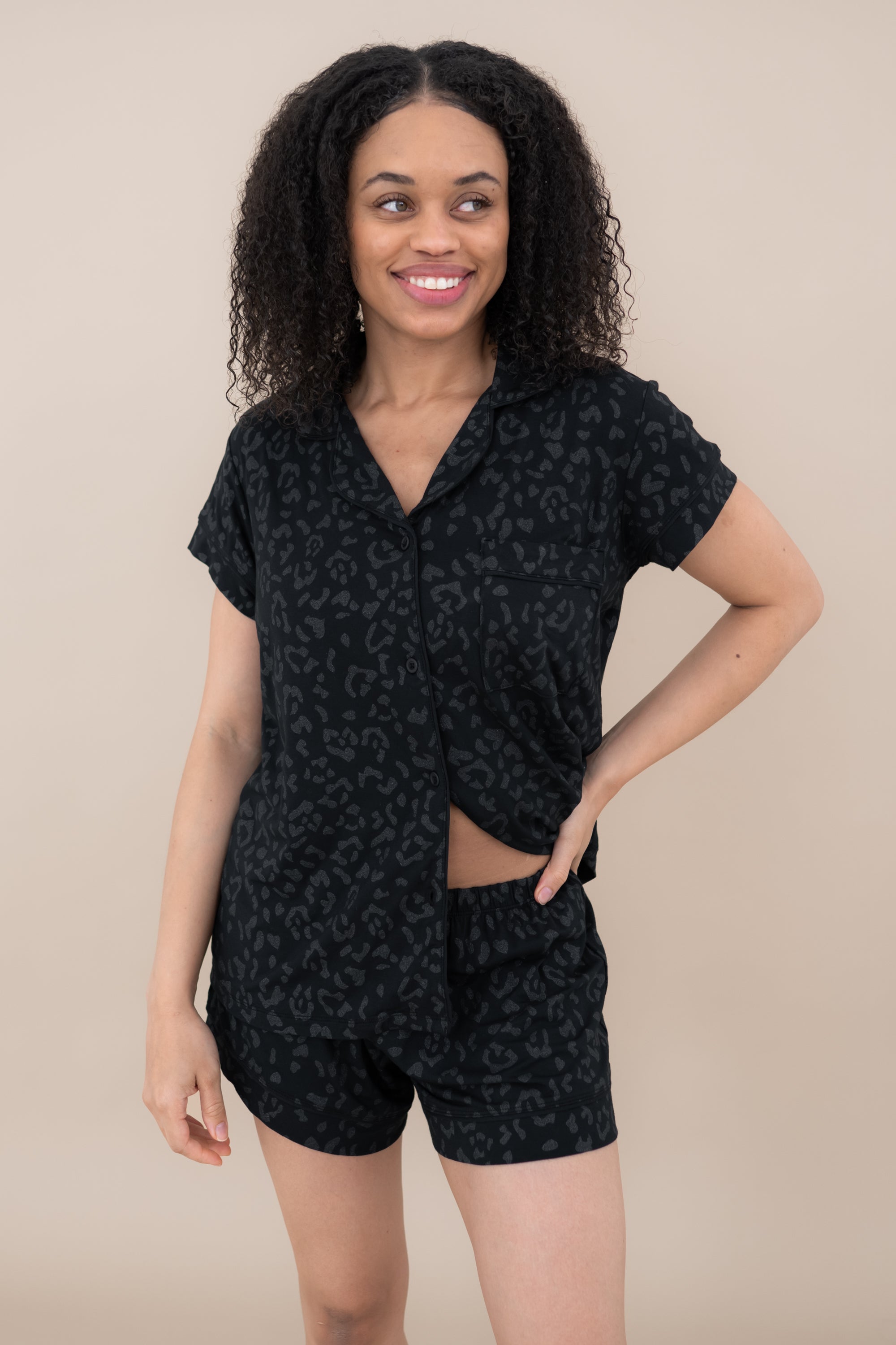 Woman modeling Women’s Short Sleeve Pajama Set in Midnight Leopard with bottom buttons unbuttoned to show the waist band of shorts