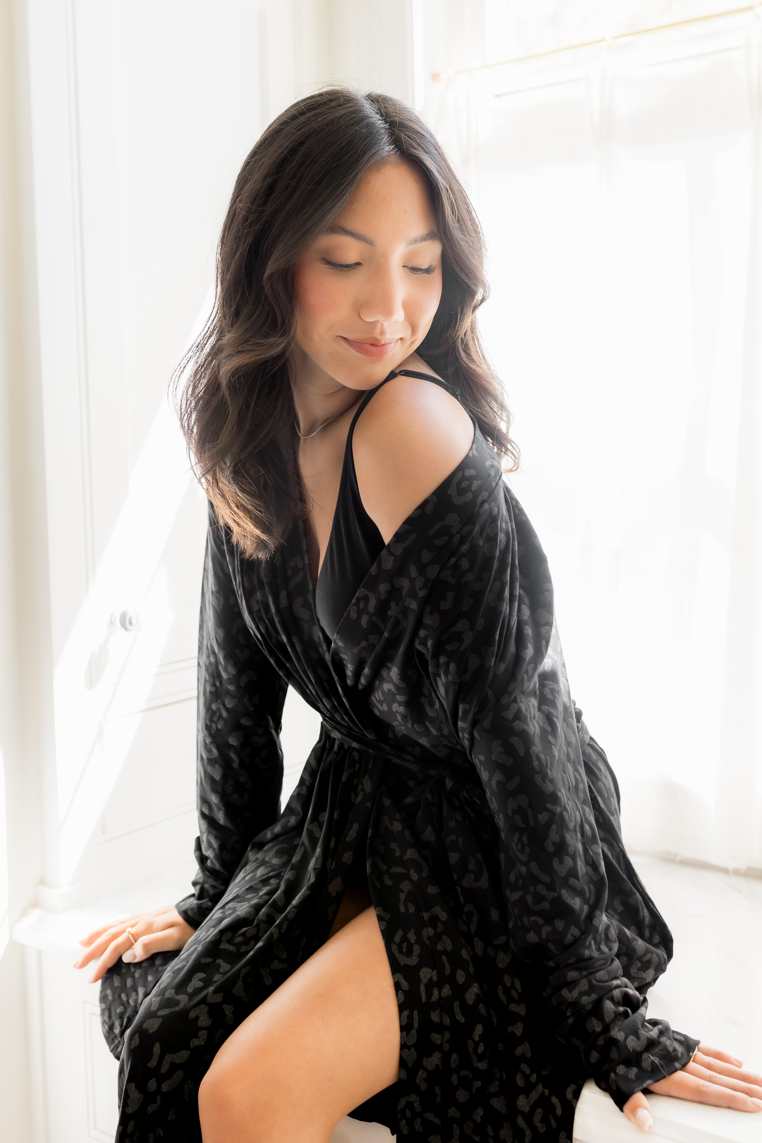 Woman wearing a black robe sitting on a white couch in a bright room.