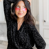 Woman wearing a black leopard print robe with pink eye masks in a bathroom setting.