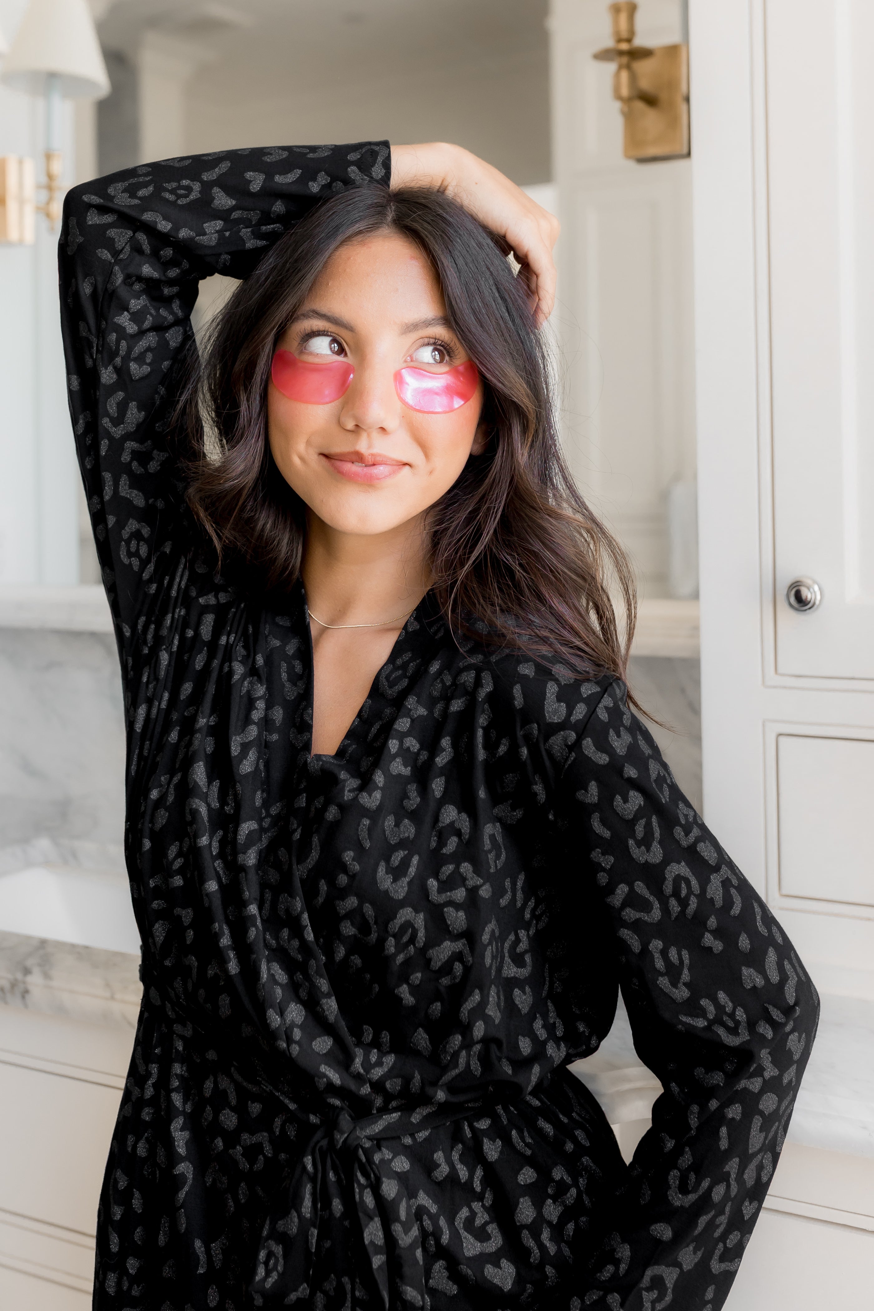 Woman wearing a black leopard print robe with pink eye masks in a bathroom setting.