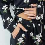 Woman modeling black long sleeve button up pajamas in a magnolia print showing waistband and pant pocket