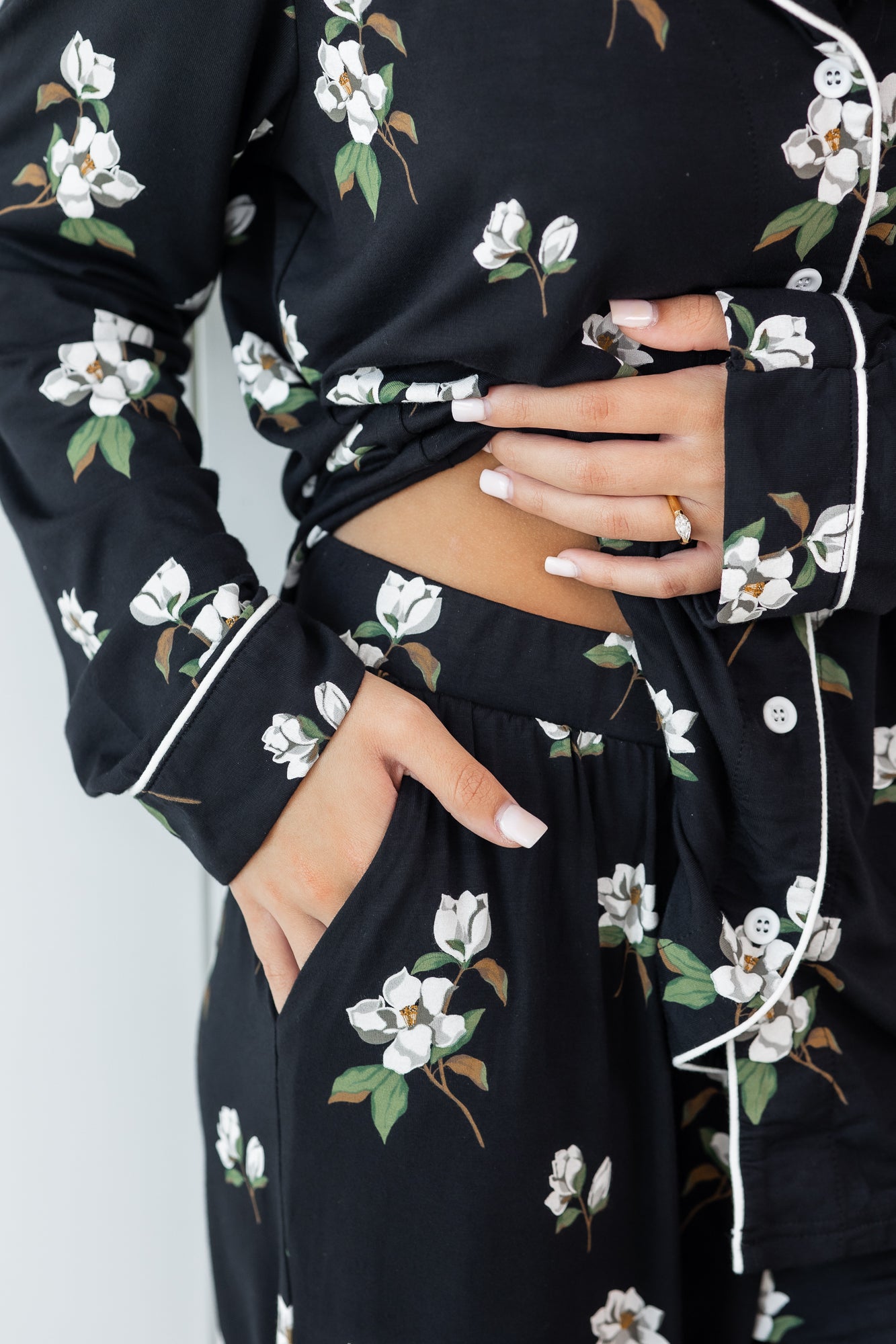 Woman modeling black long sleeve button up pajamas in a magnolia print showing waistband and pant pocket