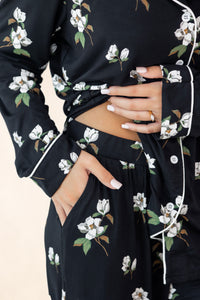 Black floral dress with white flowers and green leaves, worn by a person.