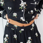 Woman modeling black long sleeve button up pajamas in a magnolia print showing waistband 