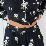 Woman modeling black long sleeve button up pajamas in a magnolia print showing waistband 
